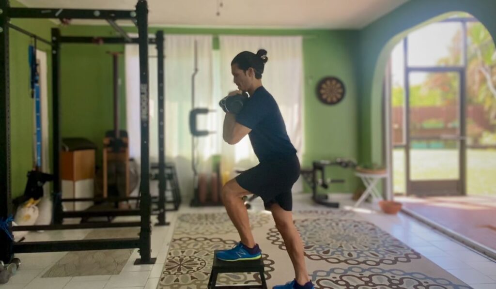 Holding the kettle bells in a front rack position strengthens the core to fight anti-flexion. In this picture a step up exercise now has an added core challenge.